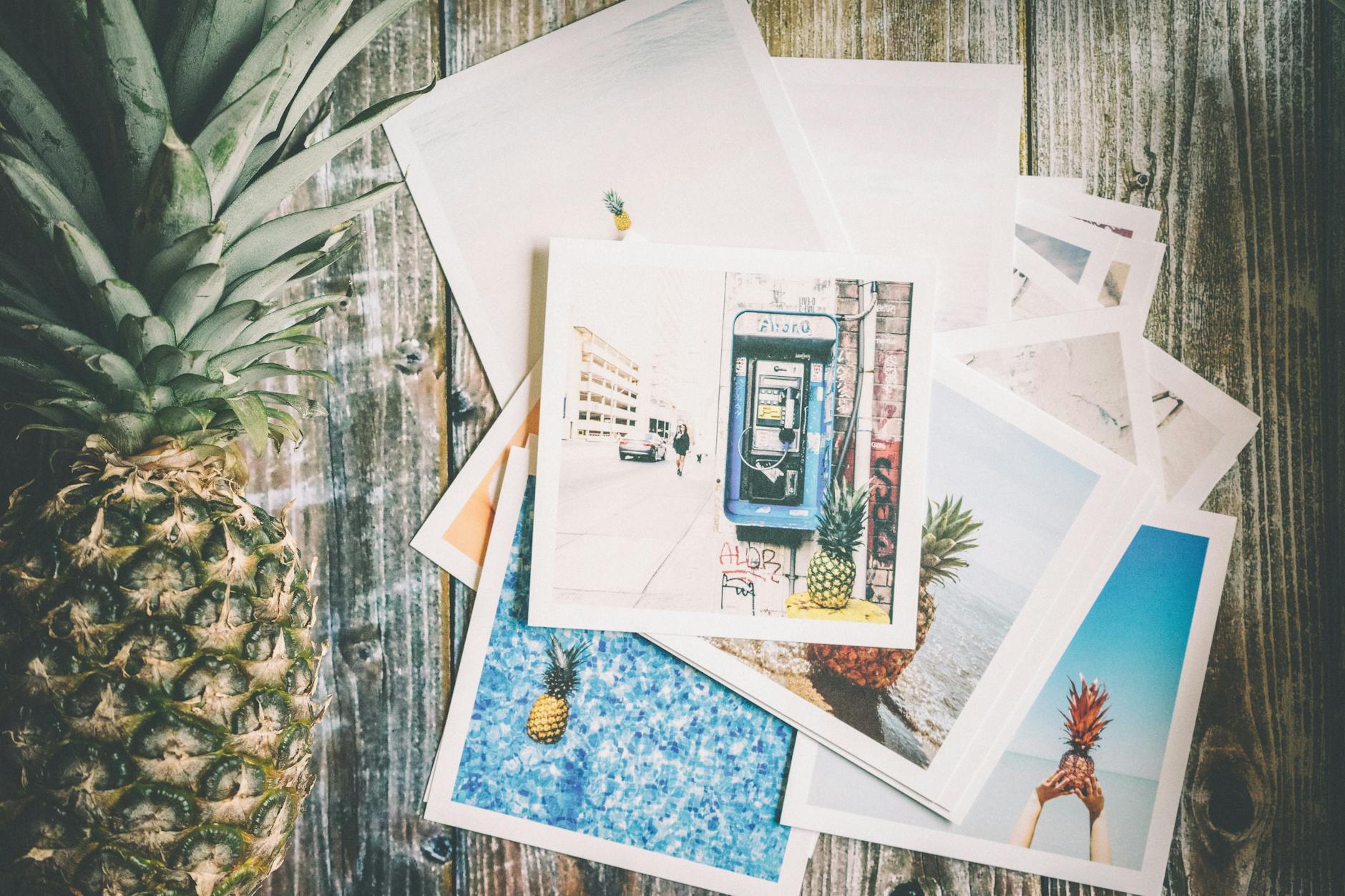 Assorted printed photo next to a whole pineapple placed on a brown surface